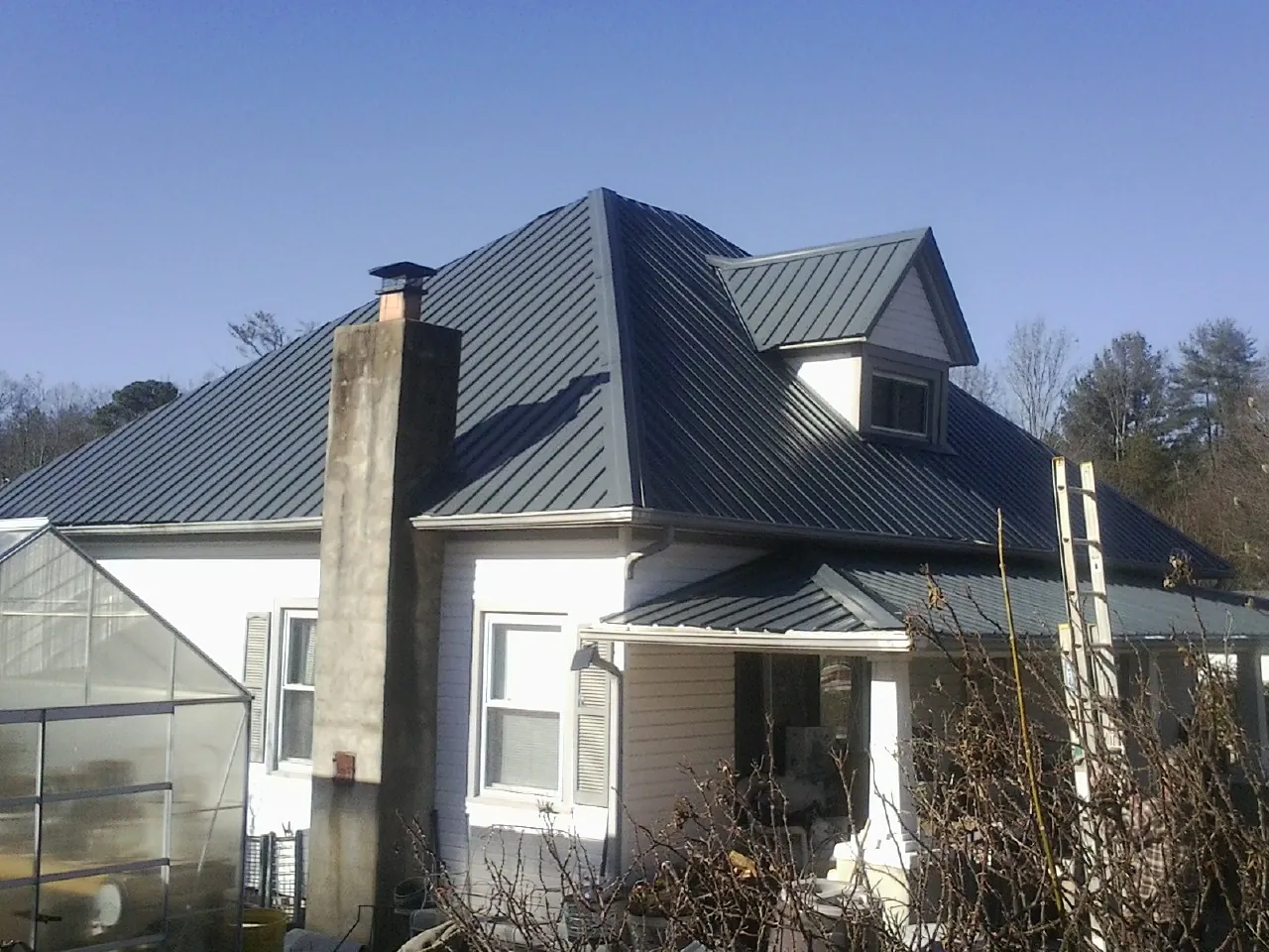 Dark blue standing seam metal roof on a white farmhouse with dormer — Slate & Tile Roof Repair by Roofing Brothers in Plummer