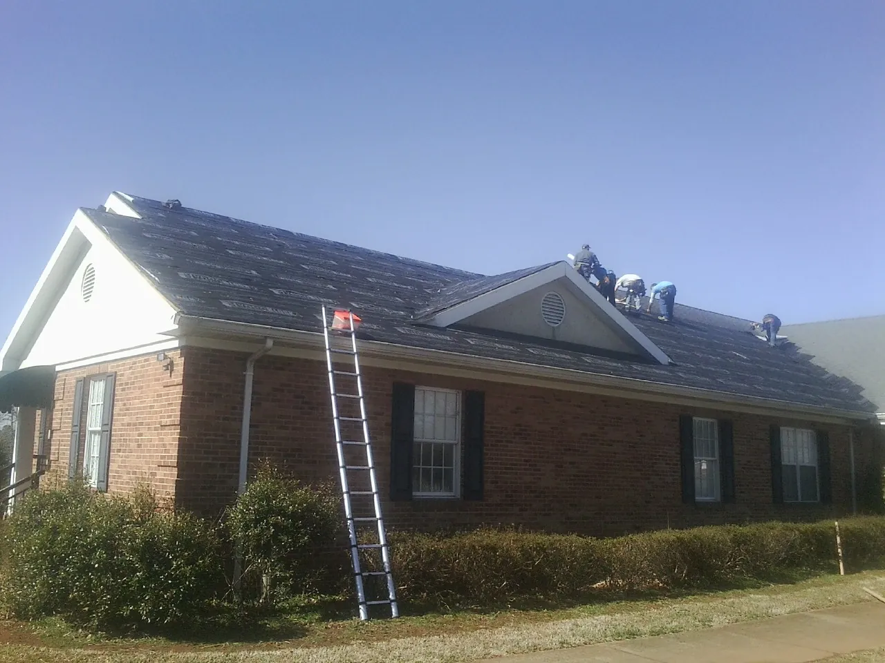 Crew tearing shingles off a brick ranch roof with a ladder set — Metal Roof Repair work by our crew in Plummer