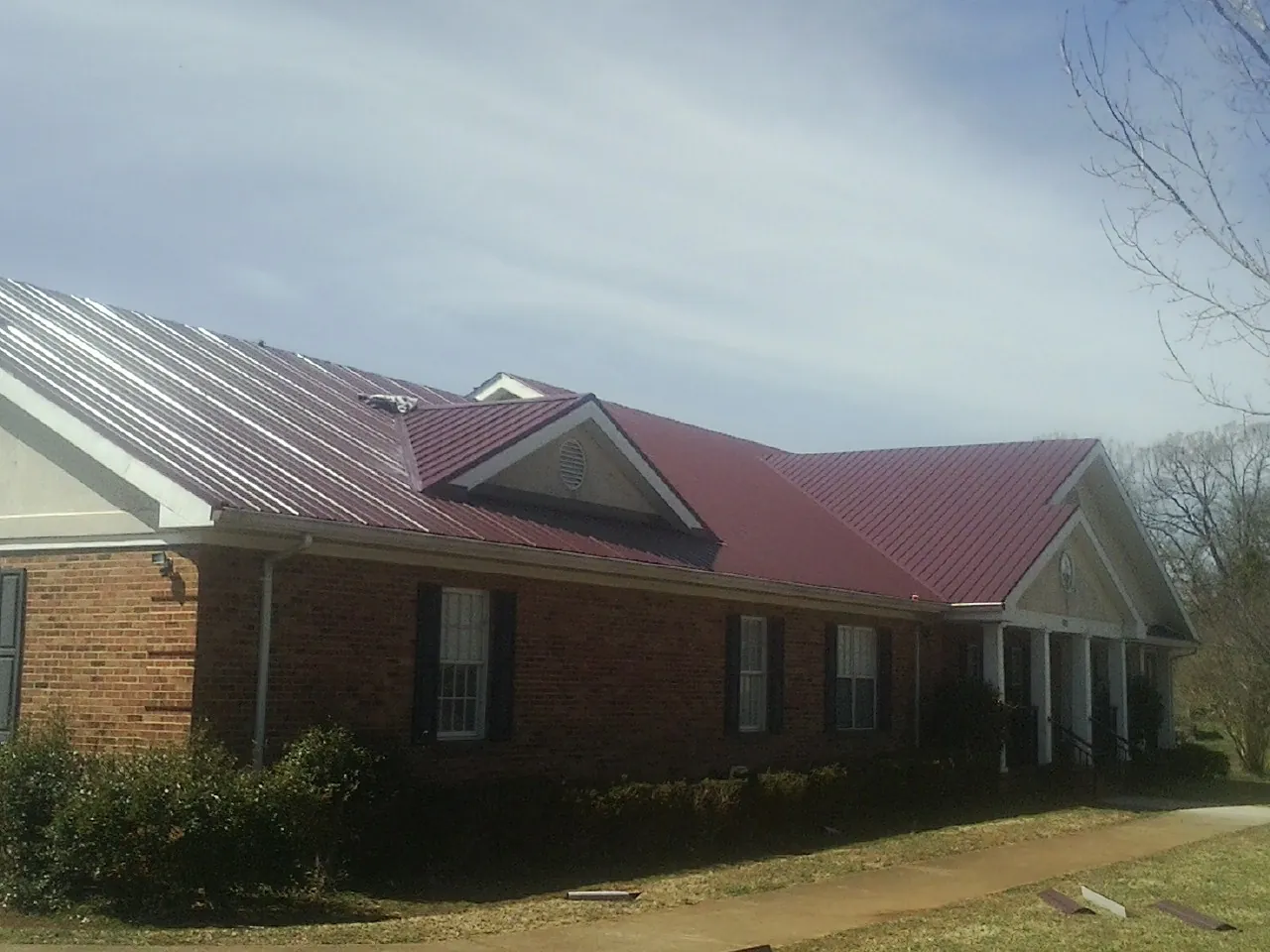Red metal roof with gabled entries on a long brick building, from a Hail Damage Roof Repair job in Plummer