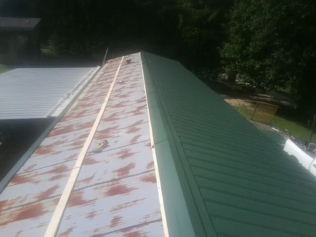 Old rusted panels beside newly installed green metal roofing — Wind Damage Roof Repair by Roofing Brothers in Plummer