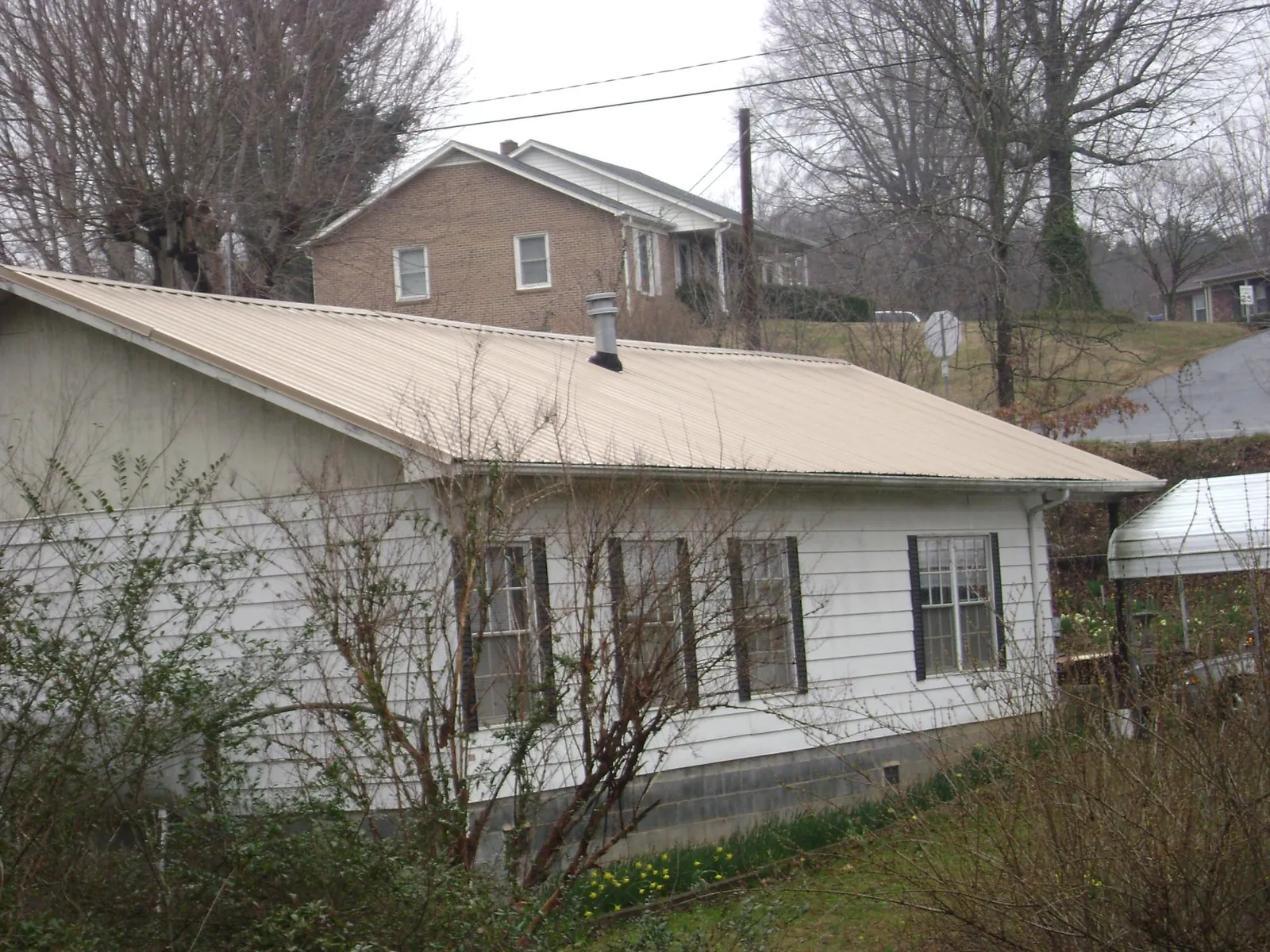 Tan metal roof on a white sided house set into a hillside — Commercial Roofing by Roofing Brothers in Plummer